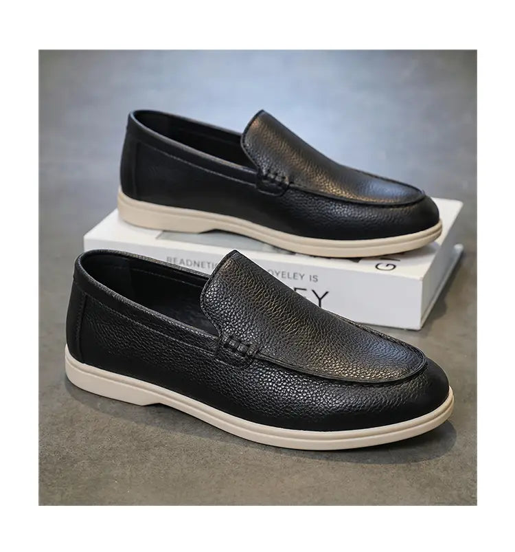 Mocassins à enfiler en cuir noir pour hommes, présentant une texture type galets et des semelles en caoutchouc blanc pour un usage décontracté.