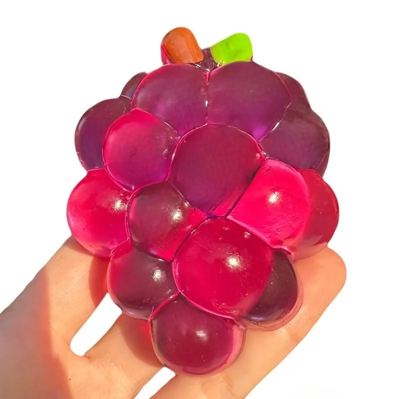 Ein transparenter, glänzender violett- und rosafarbener Trauben-geformter Stressball mit kleinem orangefarbenem Stiel und grünem Blatt, entworfen als Taba-Squishy-Grapefruit-Fidget-Spielzeug für taba-licious Fun Fruit.