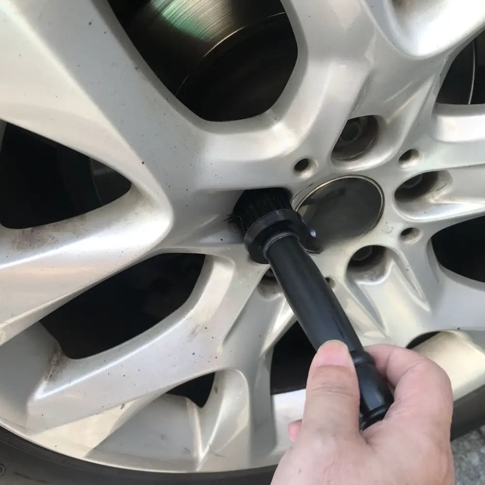 Linterna negra del conjunto de cepillos de limpieza de aros para el detalle de la rueda del automóvil, inspeccionando una rueda de aleación de aluminio plateada para una limpieza y mantenimiento exhaustivos.