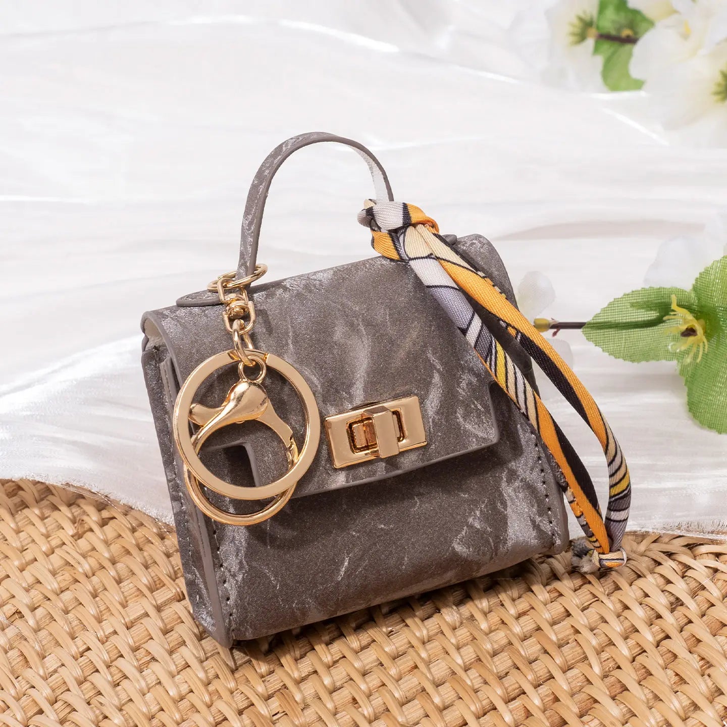 Gray textured miniature handbag keychain with gold-tone hardware and patterned silk scarf strap.