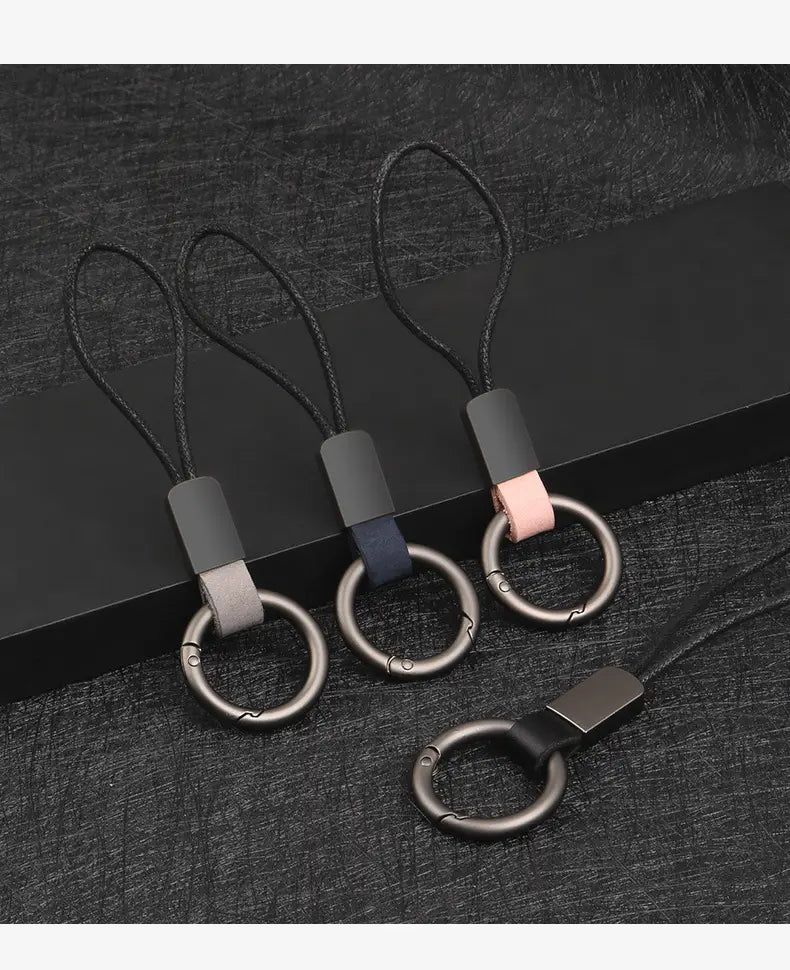 three sleek metal phone ring straps with black braided cords and color-blocked leather accents in gray navy blue and pink designed as leather keychain lanyard metal ring car key holders