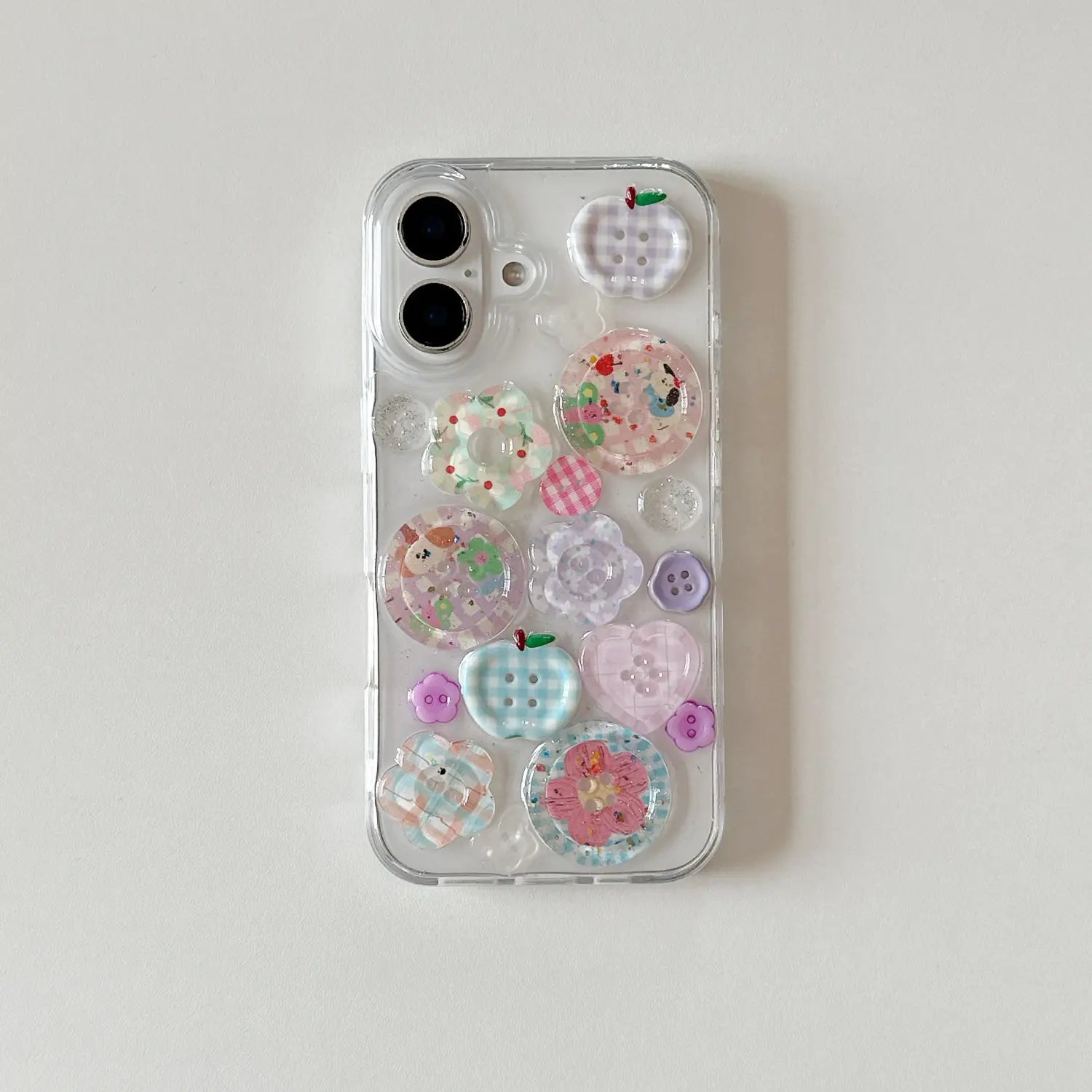 La parte posterior de una funda transparente para iPhone presenta adornos de botones translúcidos y coloridos en tonos pastel de rosa, azul y morado.