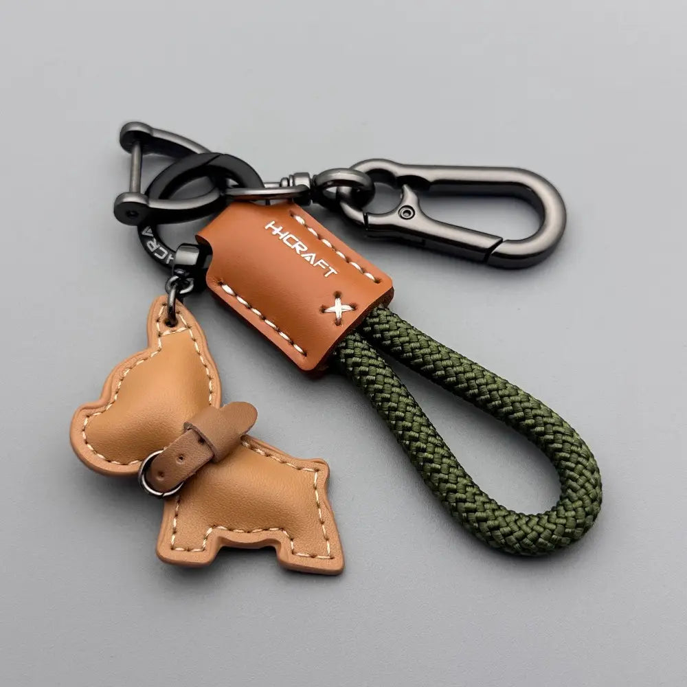 Tan leather French bulldog shaped keychain with stitched details and green braided rope loop.