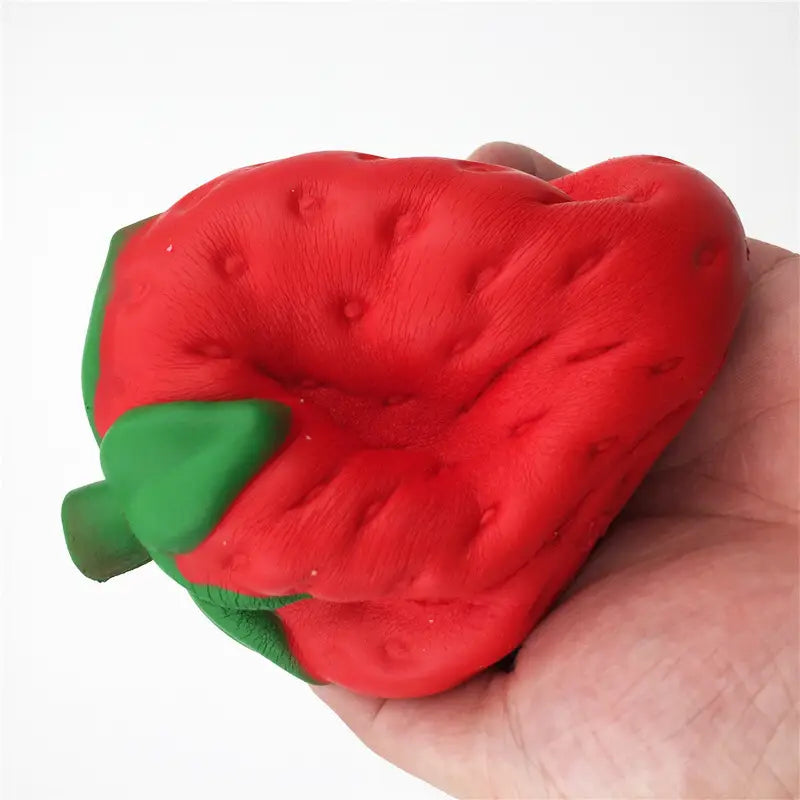 Un juguete antiestrés de fresa roja con textura, con forma de fresa, que se eleva lentamente y es blandamente esponjoso, con una parte superior de hojas verdes.
