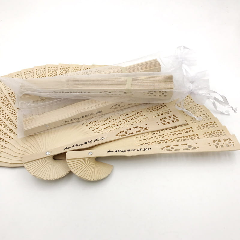 Éventails pliants en bois beige avec des découpes fines, de style dentelle, personnalisés avec des noms et une date gravés, pour des faveurs gravées en grande quantité destinées aux mariages.