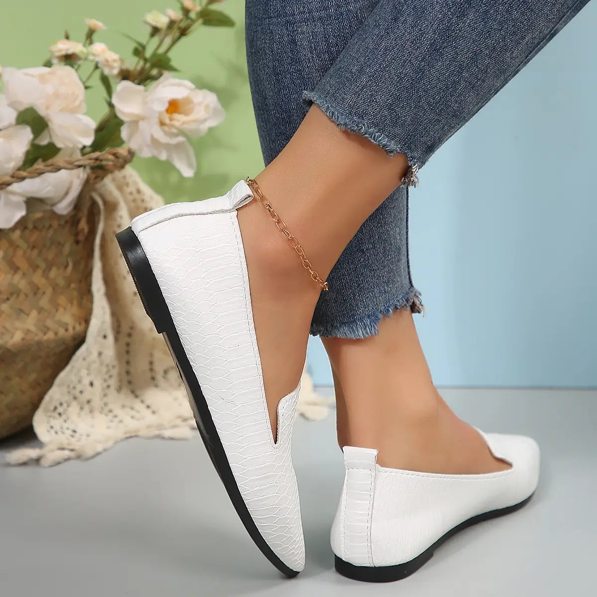 Mocasines planos de cuero con punta afilada para poner y quitar con facilidad, en cuero con relieve tipo cocodrilo blanco, con suelas negras, mostrados desde el lado posterior.