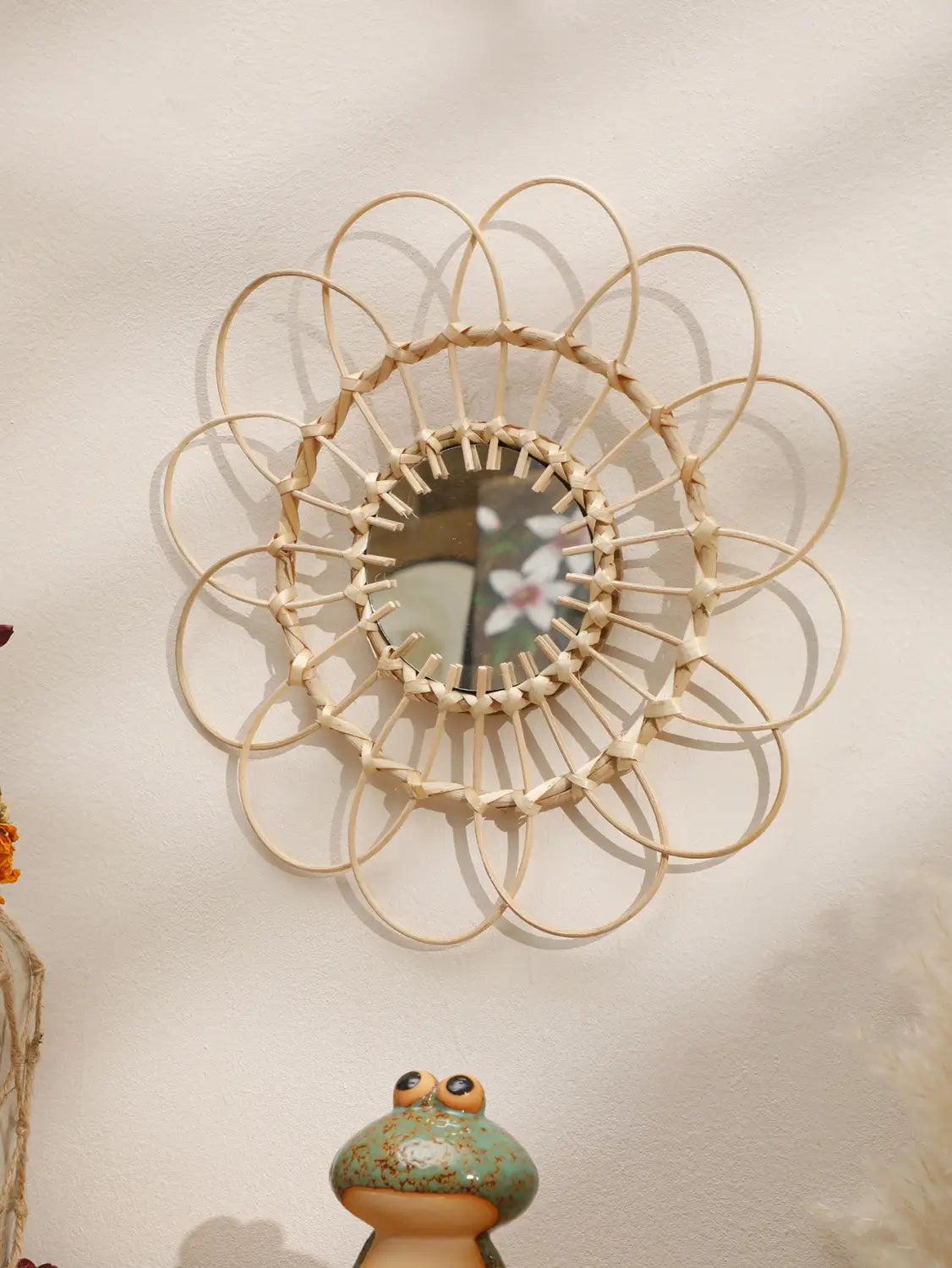 Ein runder Wandspiegel mit einem zarthellbeigen Rattanrahmen, der in einem kunstvollen Sonnenstrahlmuster angeordnet ist und ideal zur Aufwertung der ästhetischen Gestaltung des Raums dient.