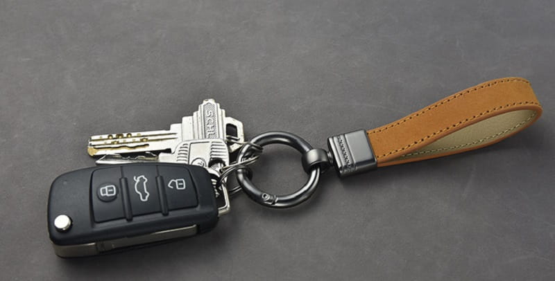 Black car key fob with silver buttons attached to a tan leather strap in a leather keychains set with multicolor metal clasp.