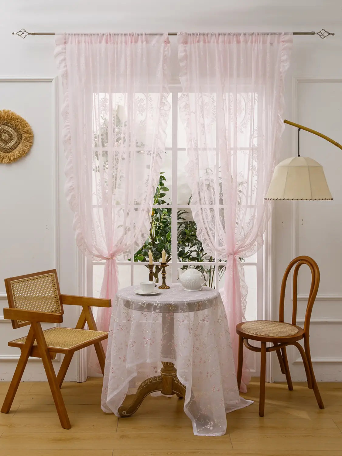 Las cortinas de encaje semitransparente rosa con delicados motivos florales y bordes fruncidos cuelgan con elegancia de una barra de soporte para espejo circular, que presenta un bolsillo para la barra a fin de facilitar la instalación.