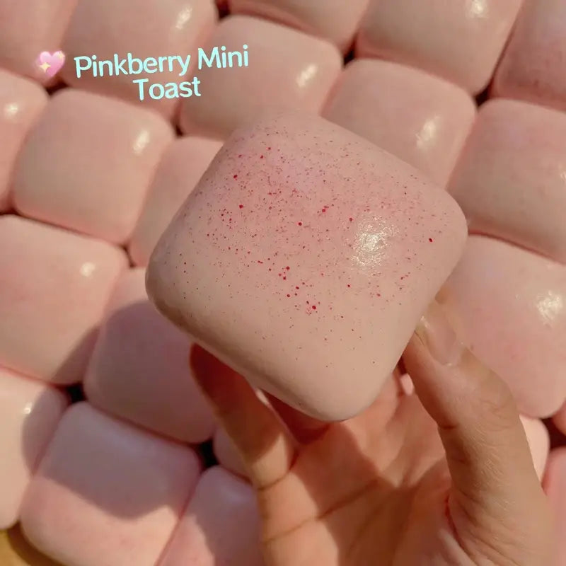 a soft pink square-shaped pinkberry mini toast slow rising squishy toy with a glossy finish and subtle red speckles designed for stress relief and sensory play