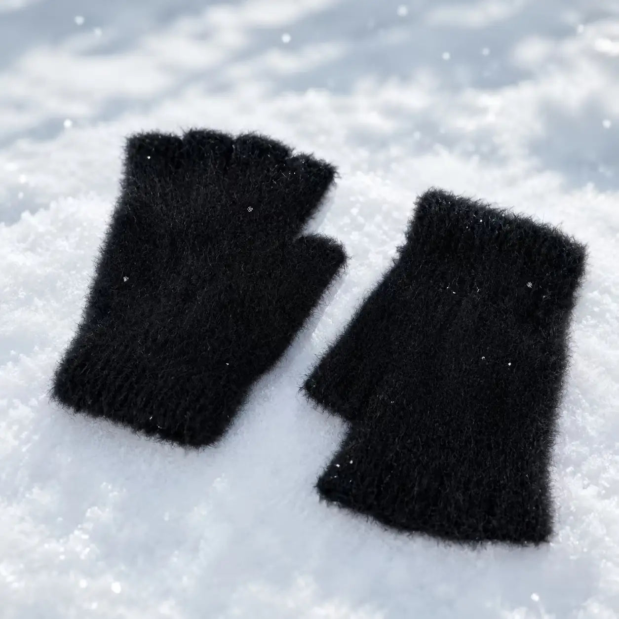 fleece-lined fingerless gloves for women in black fuzzy fabric with subtle glitter accents resting on a snowy surface