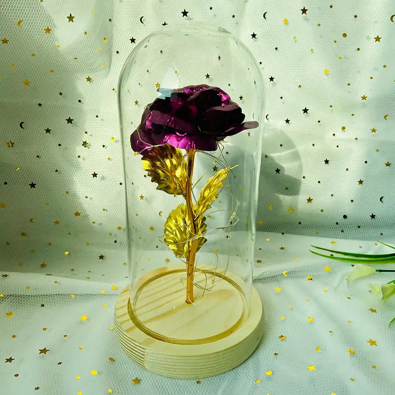 Ein schimmernder violetter Rosenblüten-Entwurf mit goldenen Blättern und Stiel, umschlossen in einer klaren Glaskuppel auf einem hellen Holzsockel, mit einem LED-Licht für ein „Eternal Gold Rose Glass Dome Gift“.