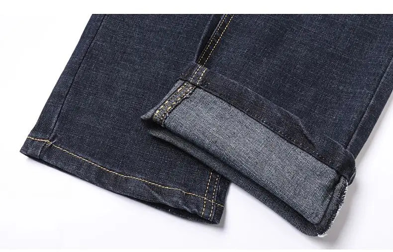 Men’s stretch cotton straight dark blue denim jeans with rolled-up cuffs revealing lighter inner lining and contrasting stitching, ideal for casual wear.