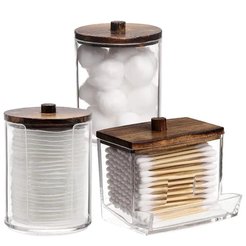 Set of three clear acrylic q-tip and cotton ball storage jars with dark wood lids designed for organized bathroom use.