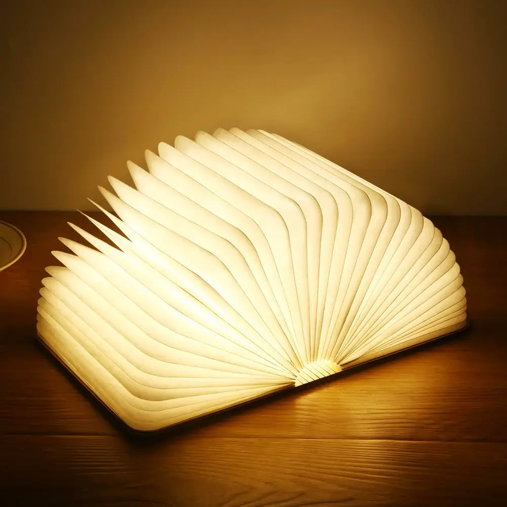 Luz LED plegable con forma de libro que emite un brillo cálido y suave, con un diseño blanco tipo acordeón plegado con elegancia, mostrada desde una vista frontal en ángulo.