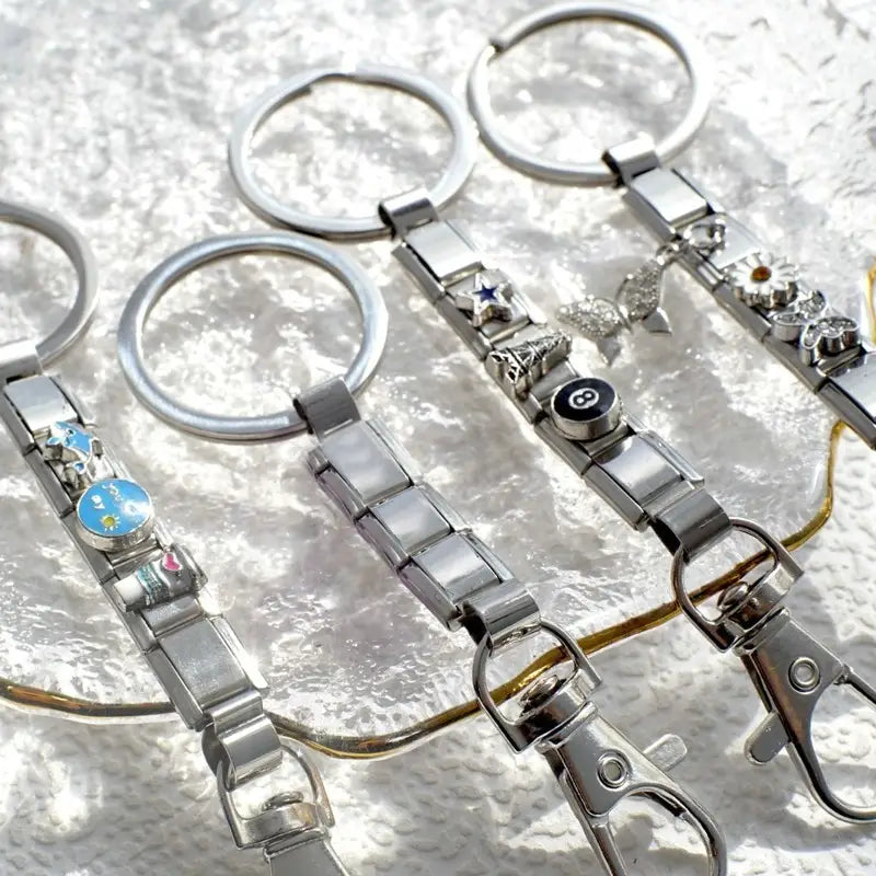 Pulseras con llavero de eslabones italianos con acabado plateado, que presentan eslabones metálicos entrelazados y dijes decorativos con estrellas, mariposas y acentos de esmalte.
