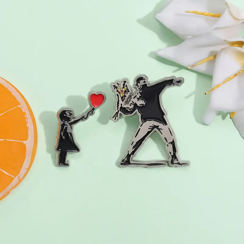 Épingle émaillée argentée mettant en scène une représentation stylisée en noir et blanc de la fille de Banksy avec un ballon, avec un ballon en forme de cœur rouge, dans un design de broche à épingle d’art de rue.