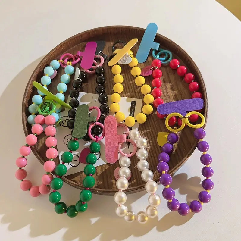 Correa de muñeca para teléfono con cuentas engarzadas que presenta cuentas de colores con dijes de letras de plástico y anillas metálicas mostradas desde un ángulo frontal.