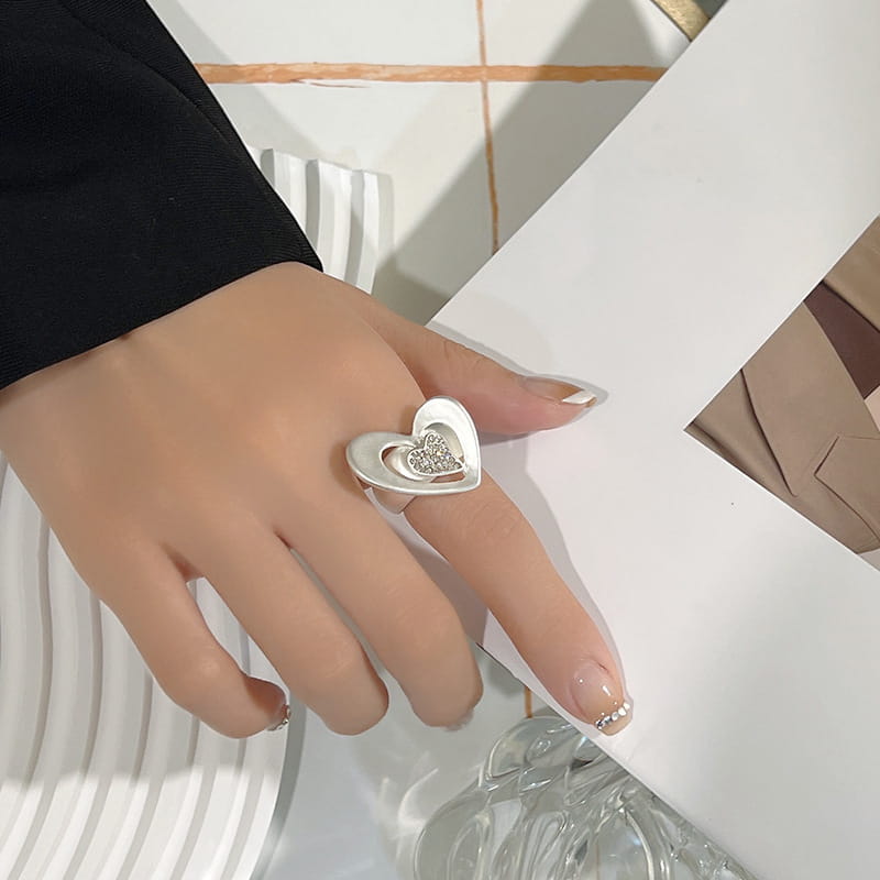 Anillo en forma de corazón en tono plata con diseño abierto ajustable, que incluye un corazón más pequeño engastado con diamantes en su interior; ideal como accesorio de joyería de anillo de corazón con pedrería.