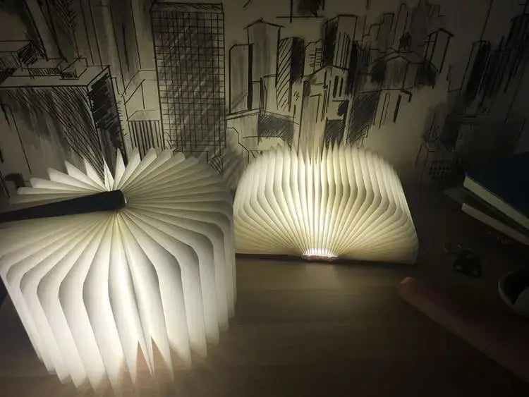 Dos luces LED plegables con forma de libro iluminadas con un brillo cálido y suave, mostrando su forma de libro abierto desde un ángulo frontal.