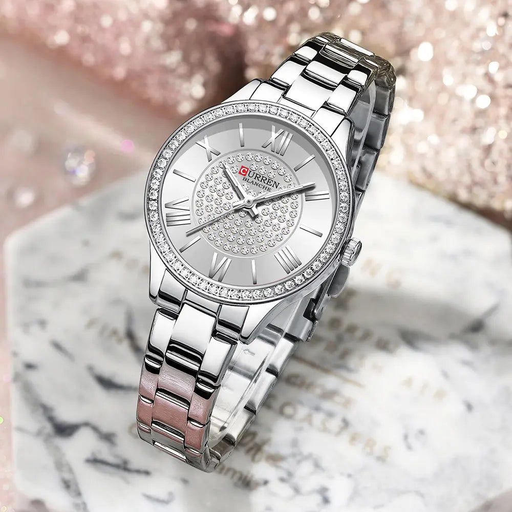 Silver-toned Curren women stainless steel crystal quartz watch with a diamond-encrusted bezel, roman numeral markers, and a sparkling crystal dial.