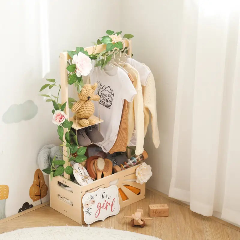 グリーンのつると白い花で飾られたベビー服ラックと、小さな棚にかぎ針編みのテディベアをのせた、ライトウッドの木製ベビーストレージバスケットの収納、保育園の装飾。