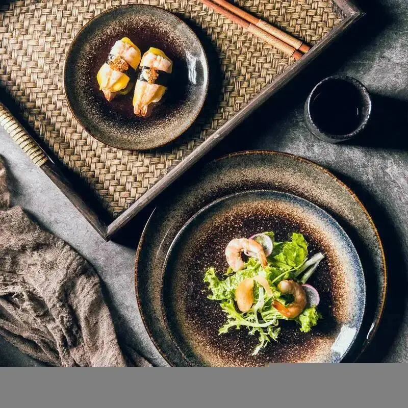 Rustic ceramic dinner plates featuring a dark speckled glaze and uneven edges designed for Japanese tableware.