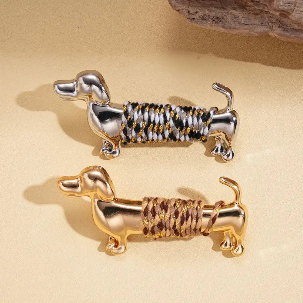 Deux porte-clés métalliques en forme de teckel, avec une finition argent et une corde tressée noir et blanc, ainsi qu’une finition ton or avec une corde tressée brun clair, conçus comme broches de teckel dorées, broches à revers animalières.