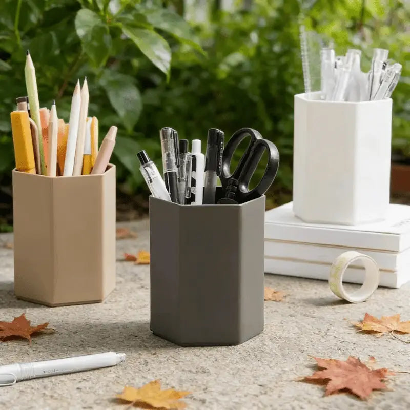 Porte-stylo en plastique hexagonal gris pour bureau, rempli de stylos et de ciseaux, afin d’organiser efficacement l’espace de travail.