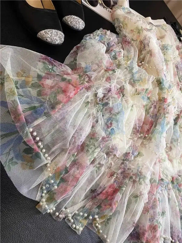 Una falda de tul floral fairycore delicada en colores pastel suaves, con tejido translúcido de múltiples capas y ribete de perlas a lo largo del dobladillo fruncido.