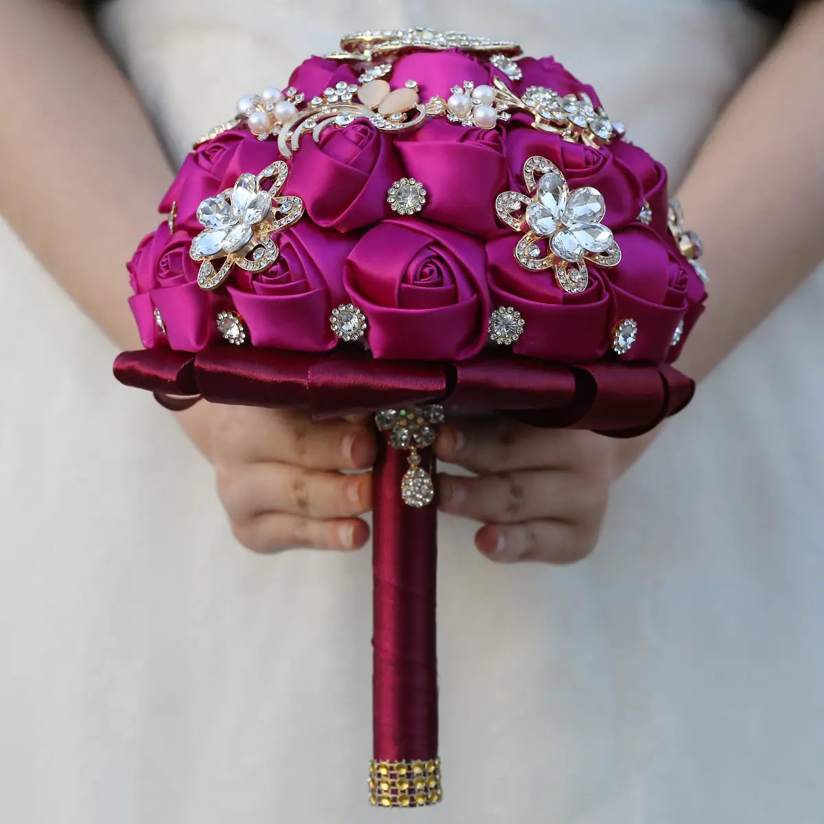 Un bouquet de mariée vibrant en satin fuchsia orné de fleurs en strass dorés étincelantes et d’accents de perles.
