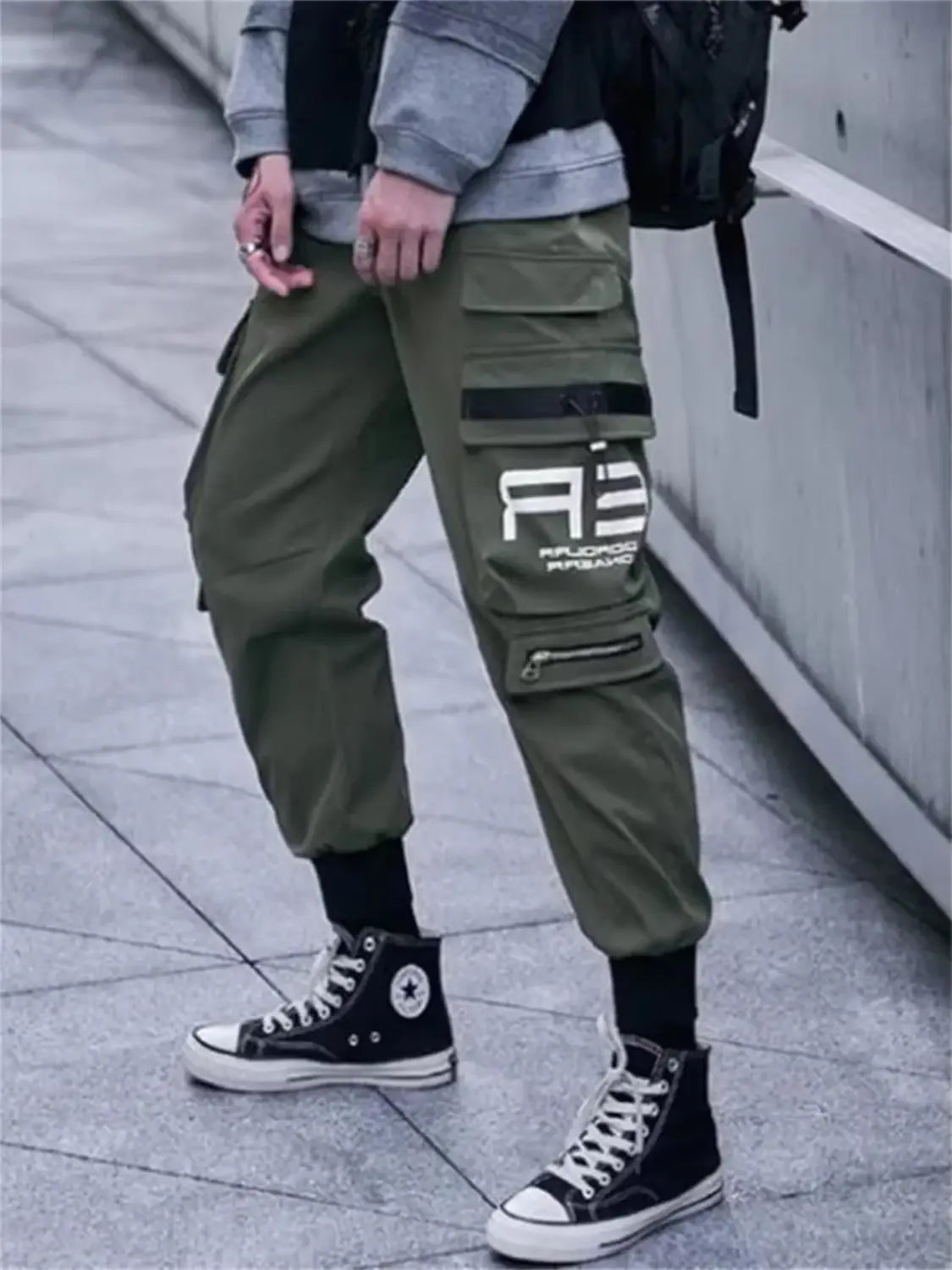 Pantalones tipo jogger cargo verde oliva para hombres con múltiples bolsillos y un logotipo blanco en el muslo, diseñados para el uso de ropa urbana y de sudaderas casuales.