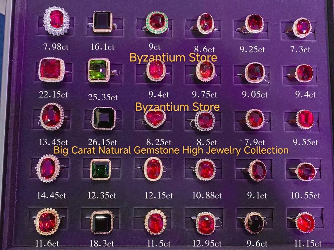 Eine Sammlung von Ringen mit leuchtend roten und grünen Edelsteinen, in goldfarbenes Metall gefasst, präsentiert auf einem violetten Samttablett mit Gewichtetiketten, neben Ohrringen mit silbernen Tropfenquasten in Gold-Vermeil.