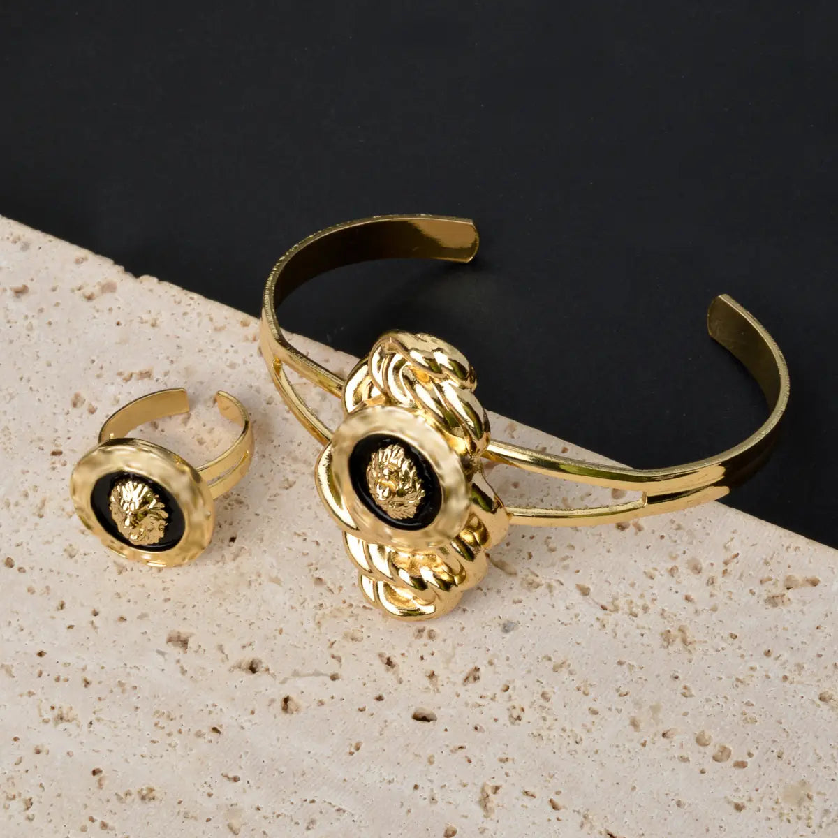 Juego de joyería de león de oro de Dubái de 18 quilates que presenta un brazalete tipo pulsera de tono dorado con un detallado intrincado tipo cuerda y aplicaciones negras, junto con un anillo a juego con aplicaciones negras.