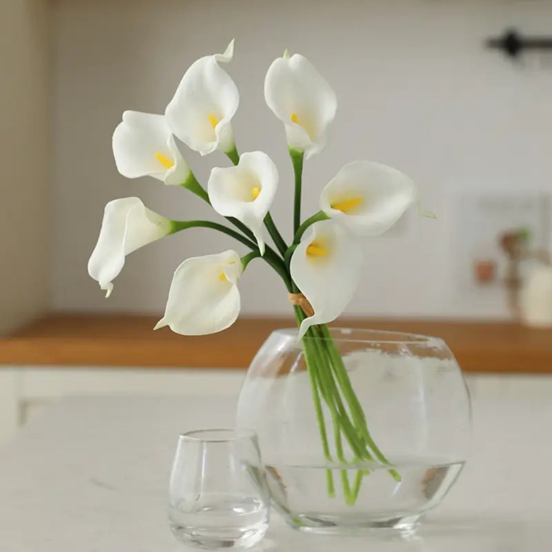 A bouquet of white calla lily flowers with yellow centers arranged in a clear glass vase for home decor.