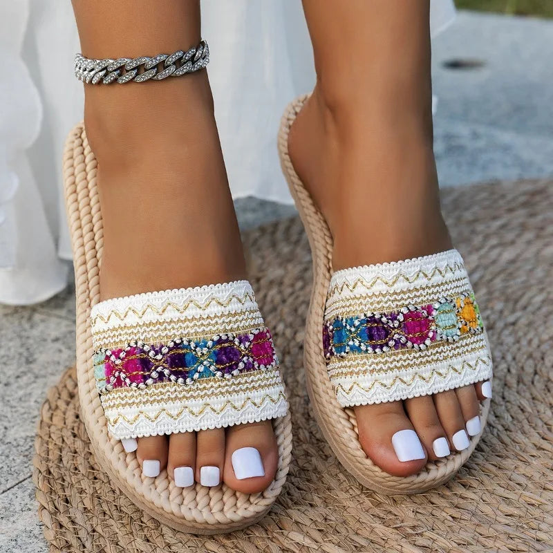 Sandalias tipo alpargata beige de tejido con correas blancas bordadas que presentan acentos decorativos con cuentas de colores y lentejuelas, diseñadas como sandalias planas bohemias con cuentas para deslizadores de verano.