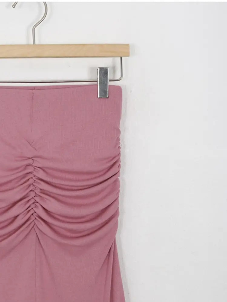 Ein zarter rosafarbener geraffter Meerjungfrauen-Midirock mit hoher Taille aus glattem Stoff, der an einem Holzkleiderbügel hängt.
