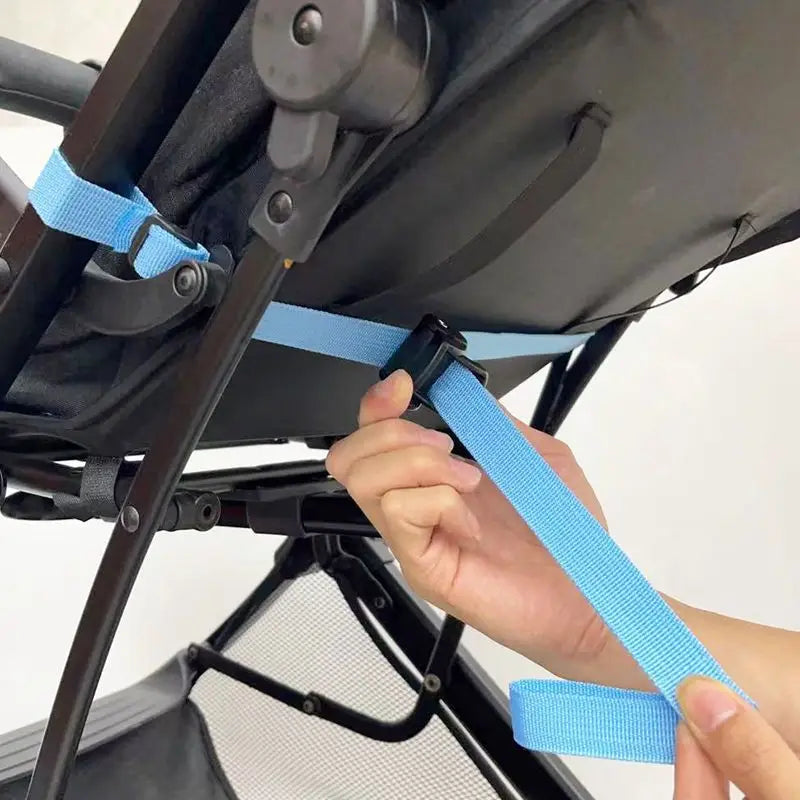 Hellblauer Nylongurt für die Rückenlehnenverstellung des Kinderwagens mit schwarzer Kunststoffschnalle, der am Rahmen eines Kinderwagens befestigt wird.