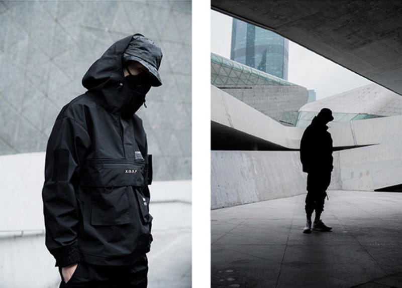 Veste imperméable à capuche tactique techwear noire, avec une poche avant et un marquage discret sur la poitrine.