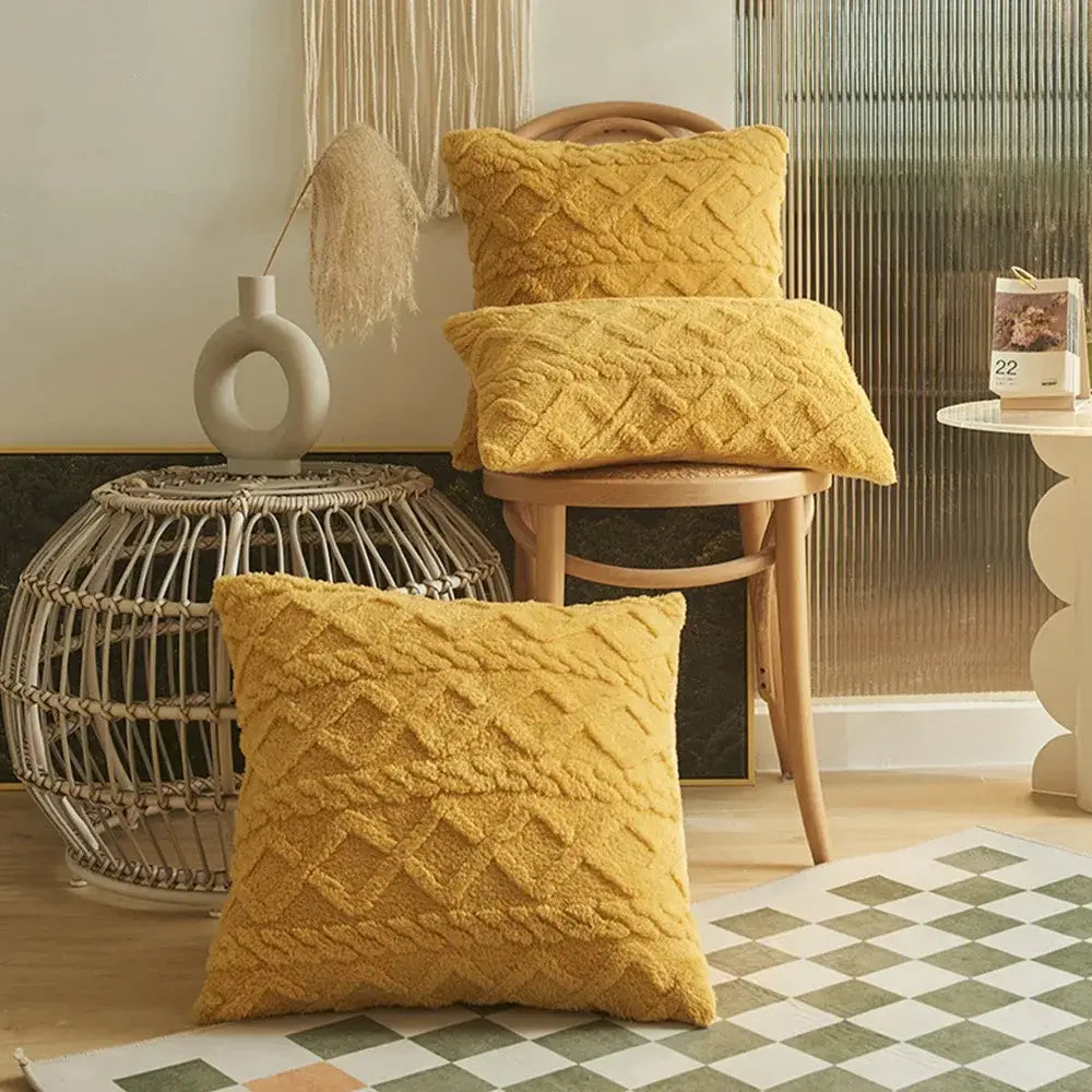 Three mustard-yellow plush geometric throw pillow covers with a diamond-knit pattern stacked on and around a wooden chair measuring 45x45cm.
