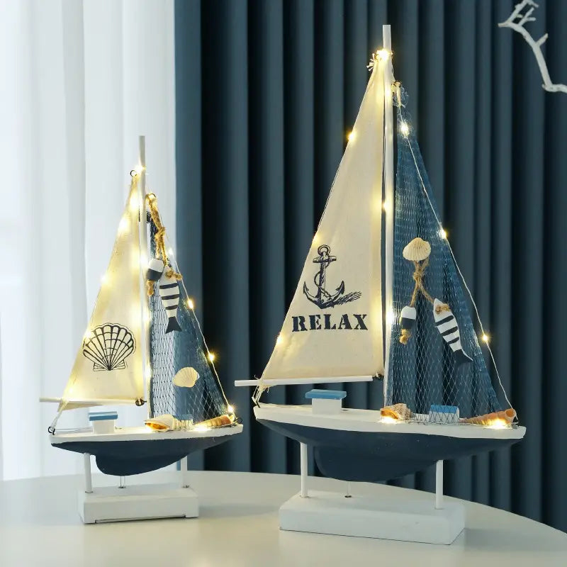 Deko im mediterranen Stil mit einer hölzernen LED-Segelboot-Dekoration für das Zuhause: maritim thematisierte dekorative Modell-Segelboote mit Segeln in Creme und Navyblau, die durch Lichterketten beleuchtet werden, sowie verziert mit Designs von Ankern und Muscheln.