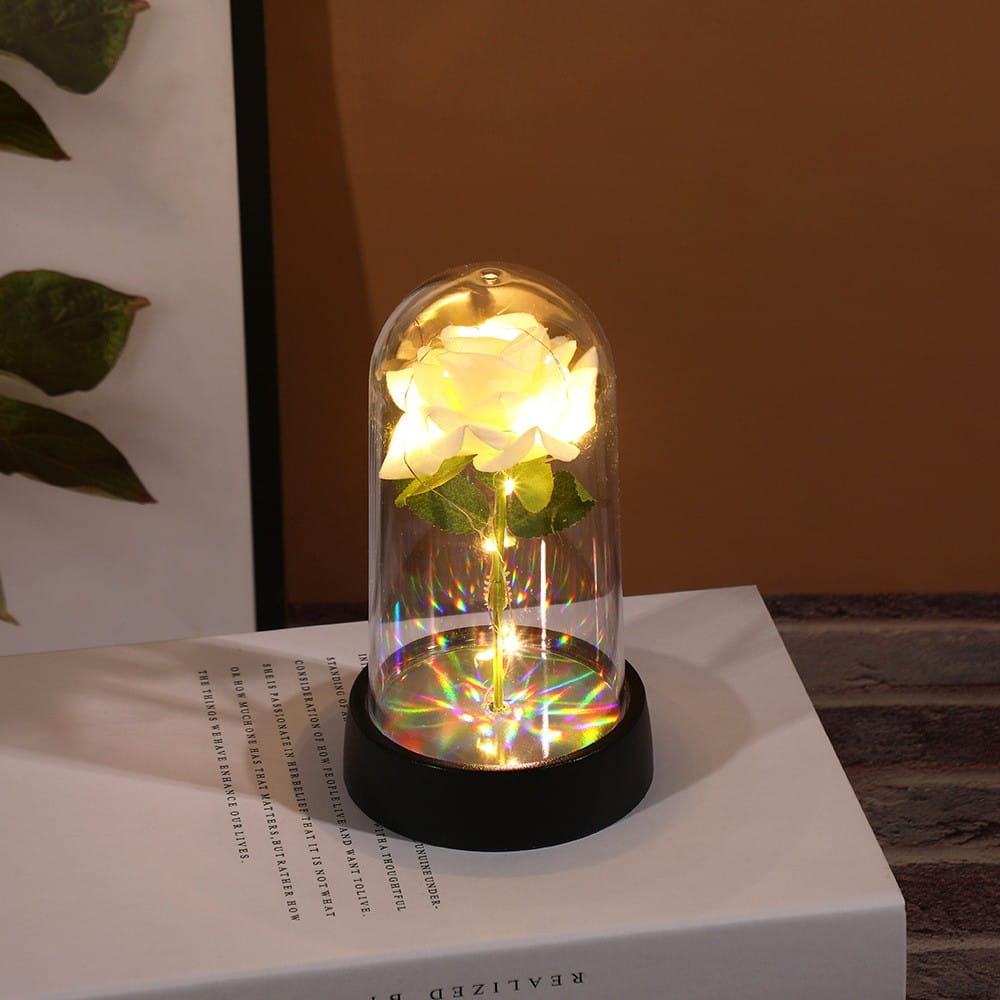 Une rose blanche luisante renfermée dans un dôme en verre transparent avec une base illuminée et des reflets de lumière arc-en-ciel dans le cadeau de fleur lumineux en dôme de rose éternelle.