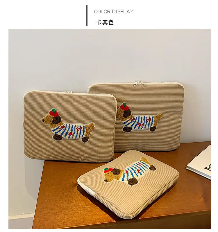 Beige Kord-Laptophülle für MacBook Pro mit einem bestickten Dackel in einem blau-weißen gestreiften Outfit und roter Mütze.