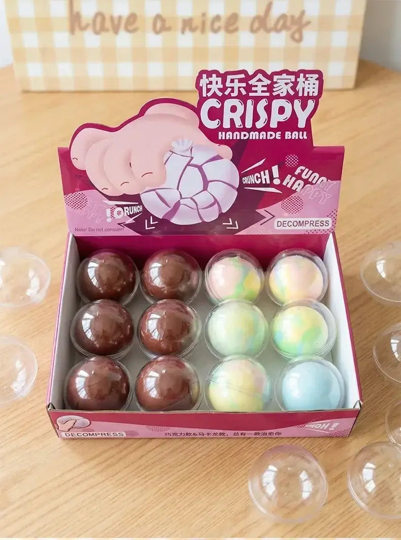 una caja de color rosa y blanco con patrón de cuadros que contiene juguetes antiestrés esféricos transparentes con piel de cera esponjosa y colores vivos, en tonos marrón chocolate y matices pastel