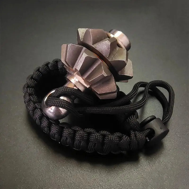A metallic, gear-shaped fidget spinner keychain with a bronze finish and black paracord bracelet designed as an emergency survival tool.