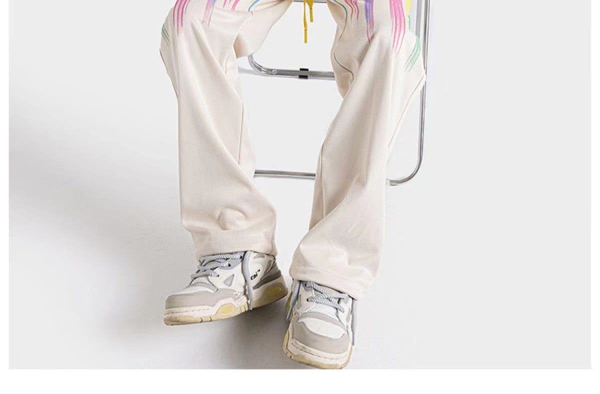 Cream-colored rainbow star graphic men sweatpants featuring wide-leg design and rainbow brushstroke detailing on the outer thighs.
