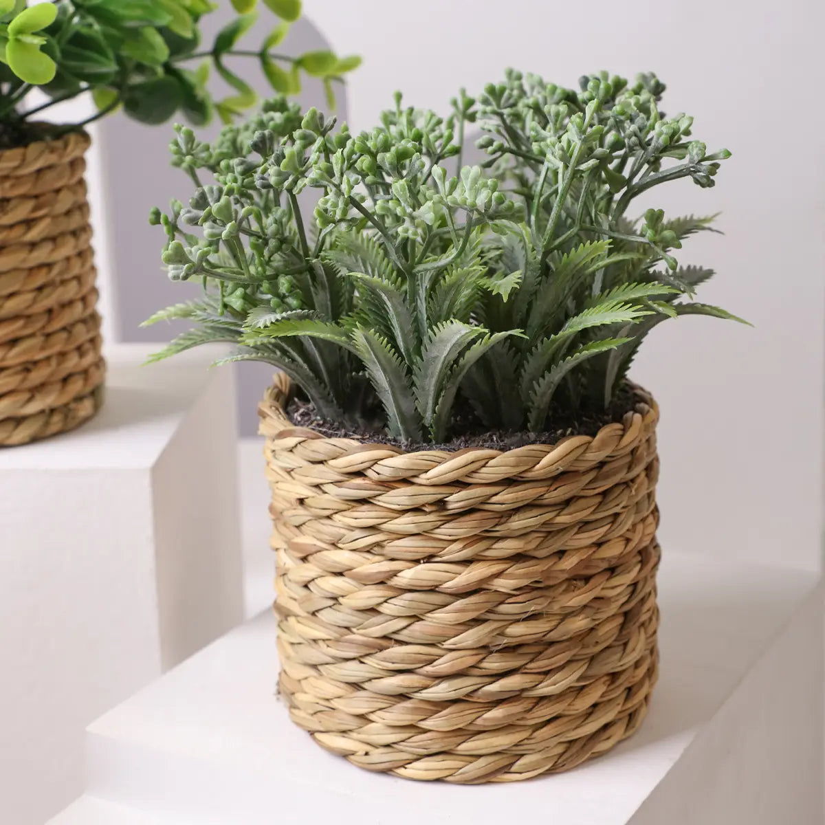 a woven natural fiber planter with a tight braided texture holds lush green artificial plants featuring small potted eucalyptus flowers measuring 17cm.