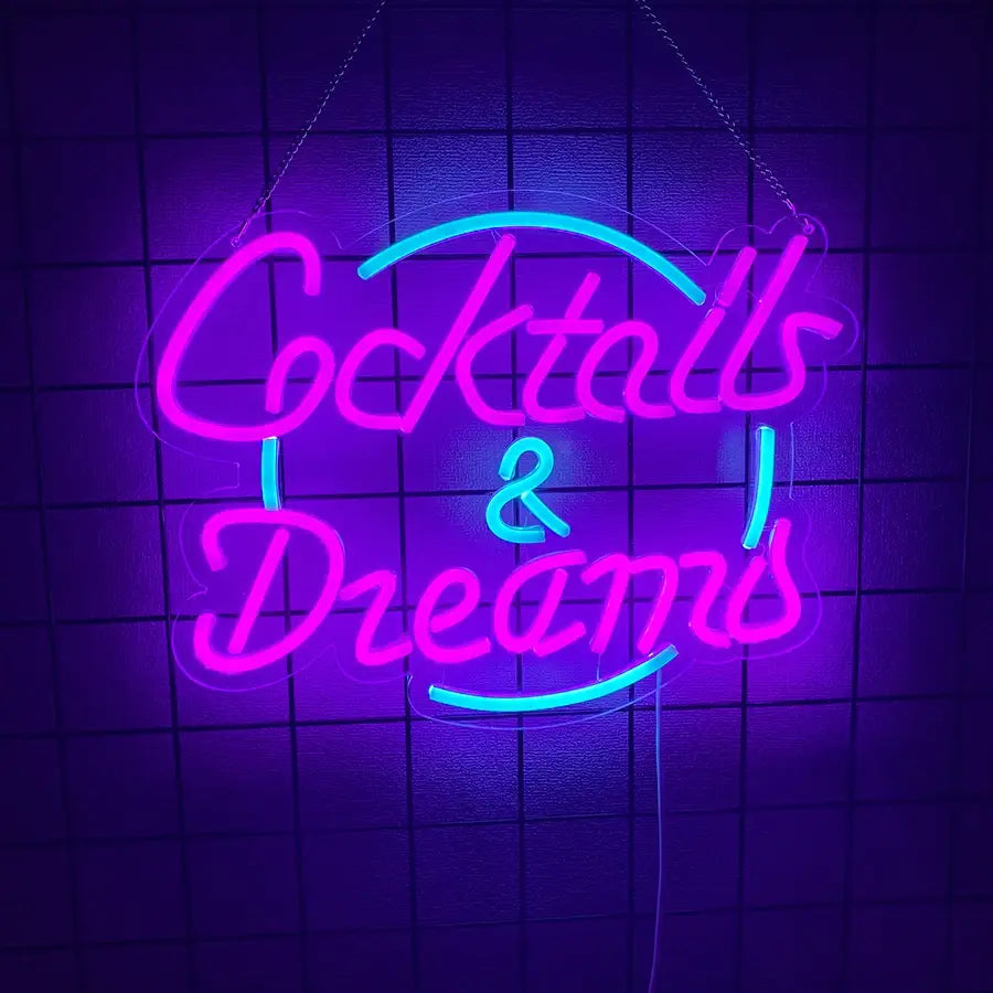 Une enseigne néon lumineuse affichant « cocktails and dreams » en tubes rose et turquoise vibrants, suspendue contre un mur sombre carrelé.