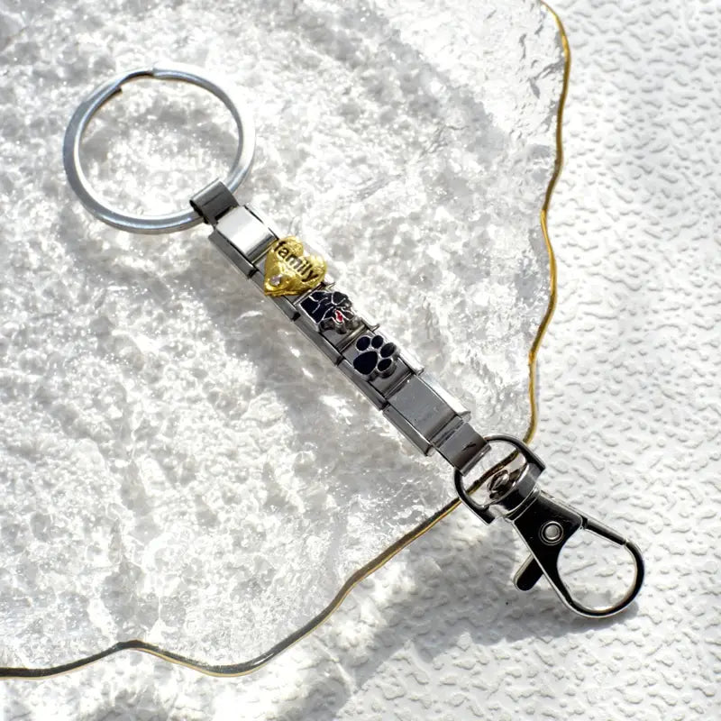 Llavero con dije de eslabones italianos con tonos plata y dorado, con un diseño modular elegante que presenta huellas de pata grabadas y un dije ornamentado grabado con la palabra «family»