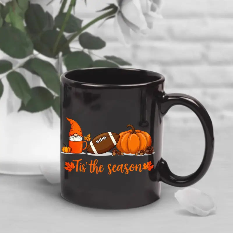 Black ceramic Easter egg coffee mug featuring a festive autumn design with an orange gnome, football, pumpkin, and the phrase tis the season in matching orange lettering.